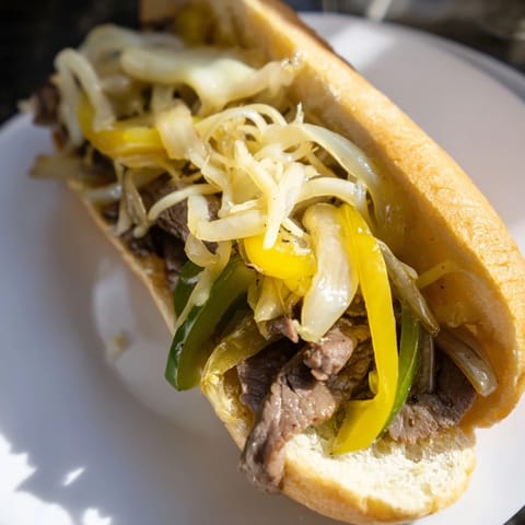 Sizzling, tender beef piled high in a Philly Cheesesteak sandwich, ready to savor.