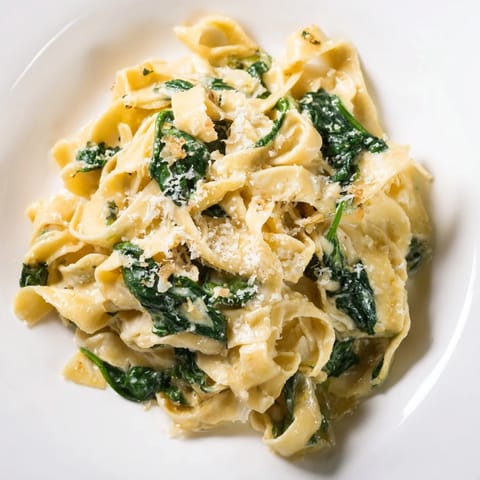 A close-up of Creamy Spinach Garlic Noodles twirled on a fork, steam rising from the rich garlic cream sauce and wilted spinach.  