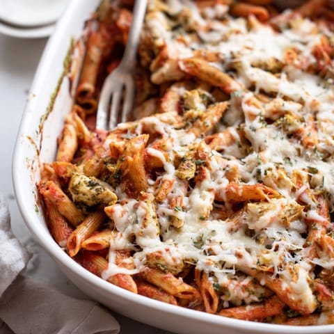 Freshly baked Pesto Chicken Pasta Bake in a white dish, garnished with basil, served alongside crisp green salad.