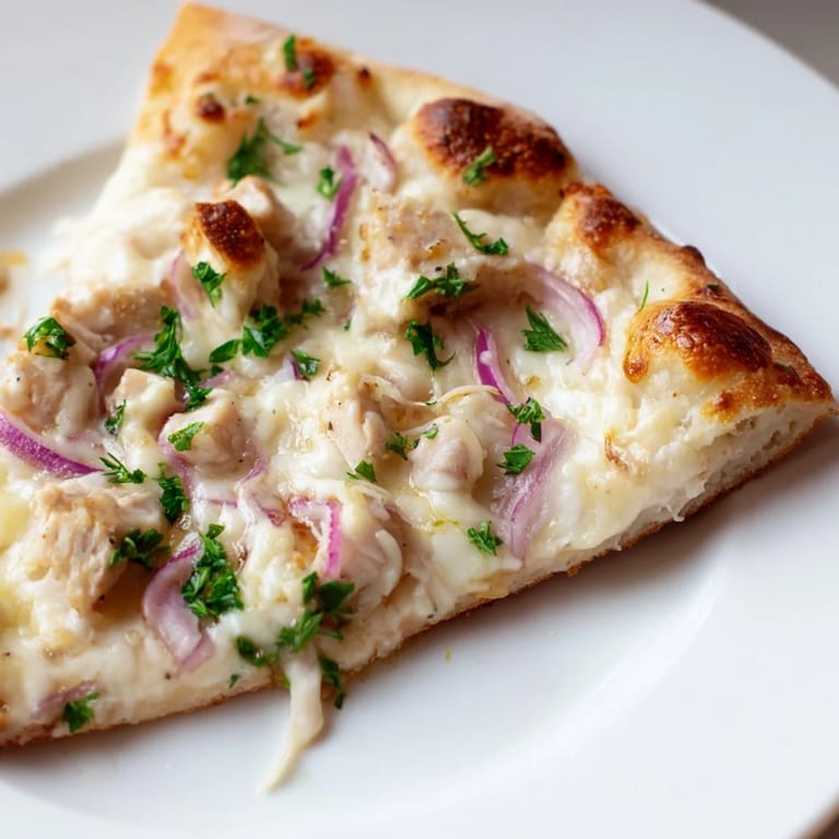 Sliced Chicken Alfredo Pizza revealing a golden crust, topped with creamy Alfredo, juicy chicken, and bubbling mozzarella on a wooden board.
