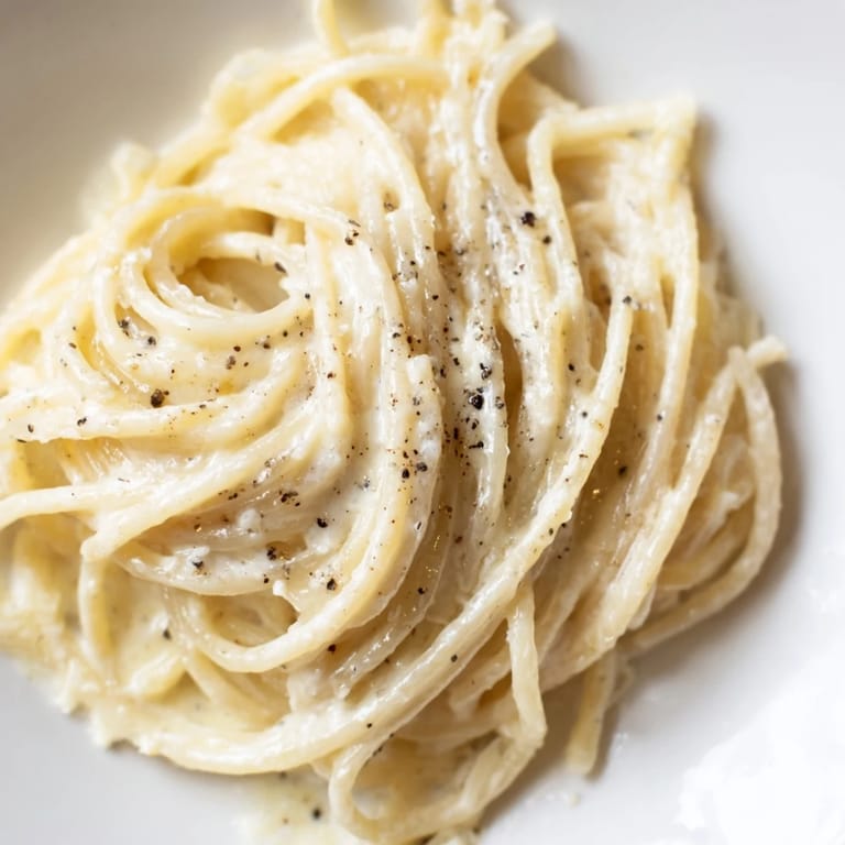 A comforting bowl of Spaghetti Cacio e Pepe served hot, garnished with extra Pecorino Romano and a glass of crisp white wine on the side.