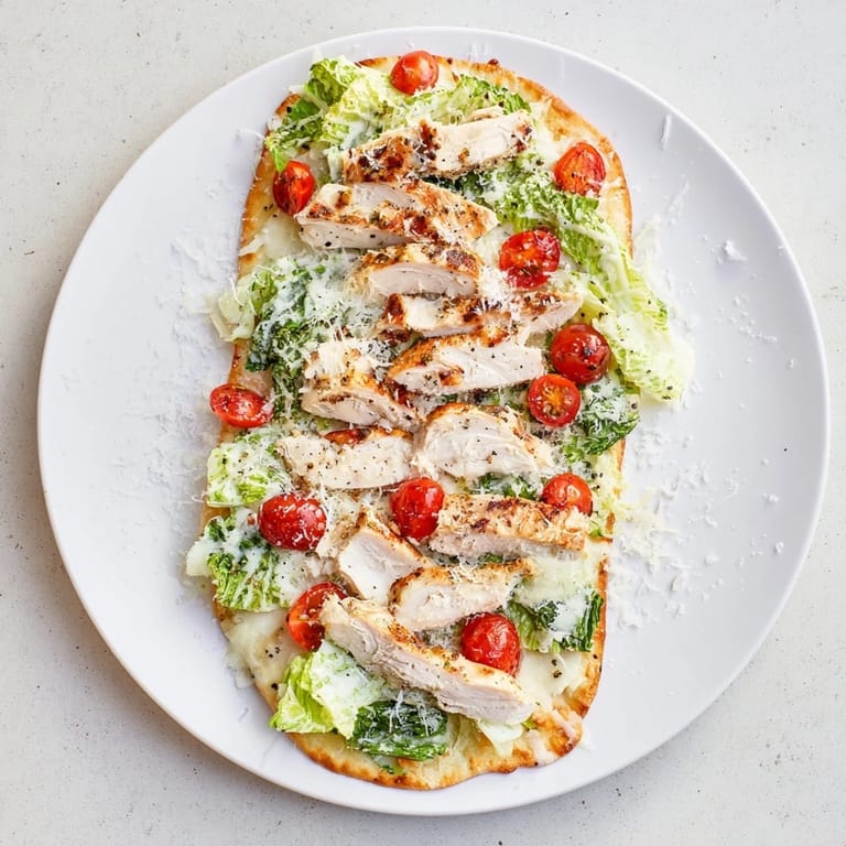 Two slices of Caesar Chicken Flatbread served with lemon wedges, showcasing fresh romaine and melted Parmesan on naan.  