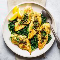 Golden pan-seared Spinach Lemon Butter Chicken cutlets resting on a bed of wilted greens, drenched in a bright, glossy lemon butter sauce.