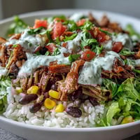 Carnitas Burrito Bowl with tender slow-cooked pork, fluffy rice, and zesty lime crema on a speckled ceramic bowl.